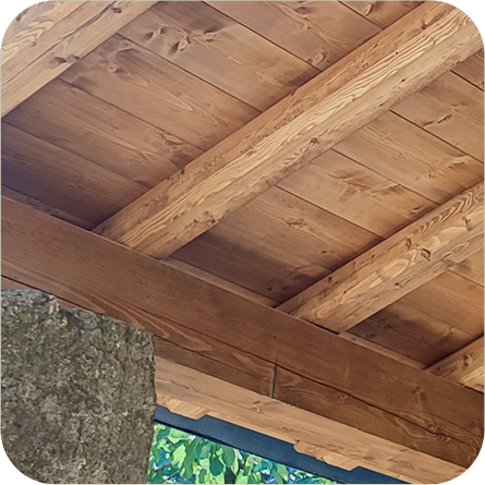 Tettoia in legno con travi a vista, che mostra la texture naturale del legno e i dettagli strutturali.