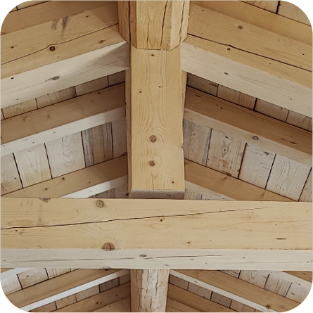 Dettaglio di un soffitto in legno chiaro con travi portanti incrociate, che mostra la struttura robusta e la naturalezza del materiale.