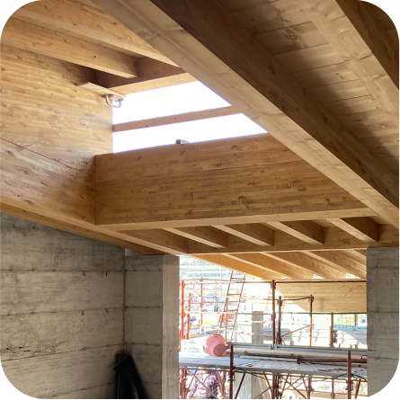 Struttura interna in legno di un edificio in costruzione, con travi e soffitto in legno che creano uno spazio aperto e luminoso.