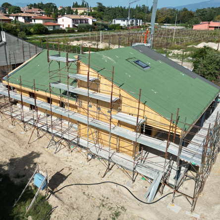 Costruzione di una casa in legno con impalcature, tetto verde e pannelli solari visibili in una zona residenziale.